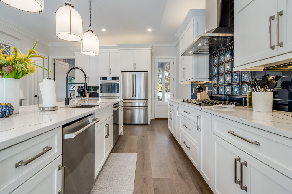 Inspiration for a mid-sized coastal light wood floor eat-in kitchen remodel with a drop-in sink, white cabinets, wood countertops, blue backsplash, stainless steel appliances, an island and white countertops