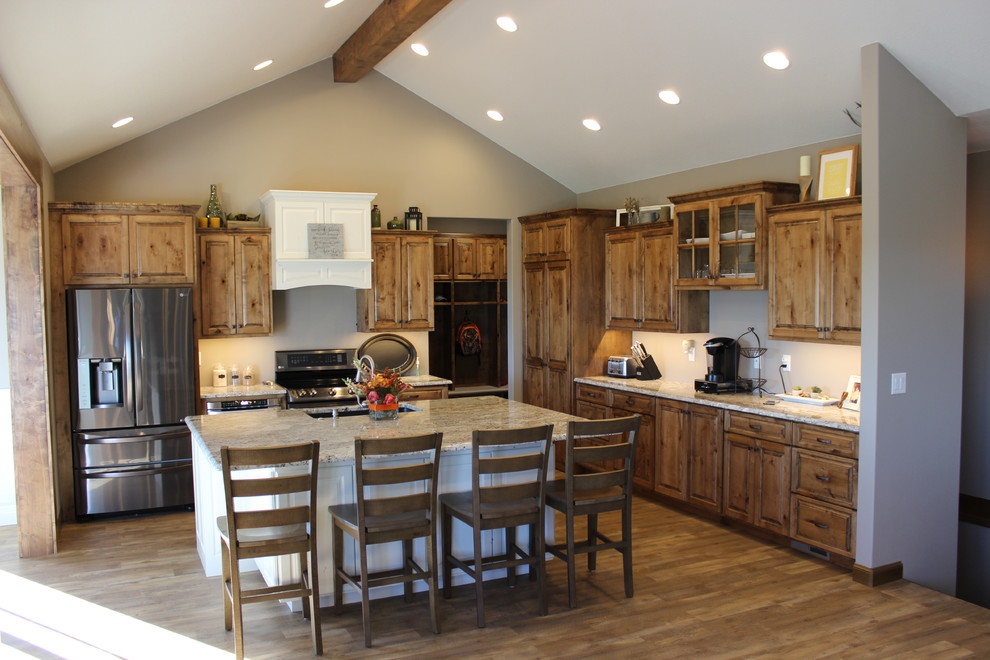 Large mountain style l-shaped medium tone wood floor and brown floor open concept kitchen photo with an undermount sink, raised-panel cabinets, medium tone wood cabinets, granite countertops, stainless steel appliances and an island