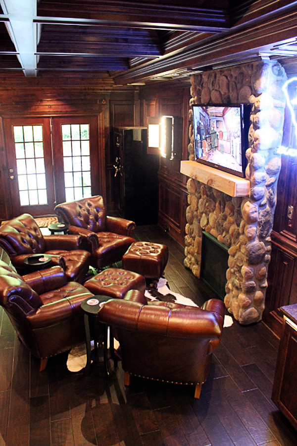 Basement - mid-sized rustic walk-out dark wood floor and brown floor basement idea with brown walls, a standard fireplace and a stone fireplace