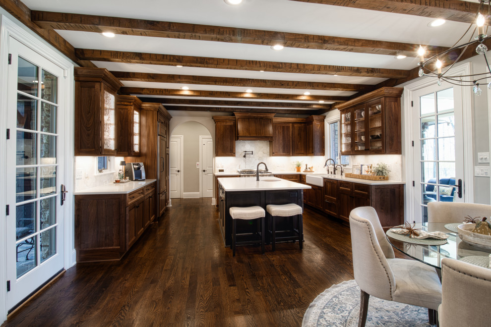 This is an example of a mid-sized transitional u-shaped eat-in kitchen in Nashville with a farmhouse sink, shaker cabinets, medium wood cabinets, quartz benchtops, multi-coloured splashback, marble splashback, panelled appliances, medium hardwood floors, with island, brown floor, white benchtop and exposed beam.