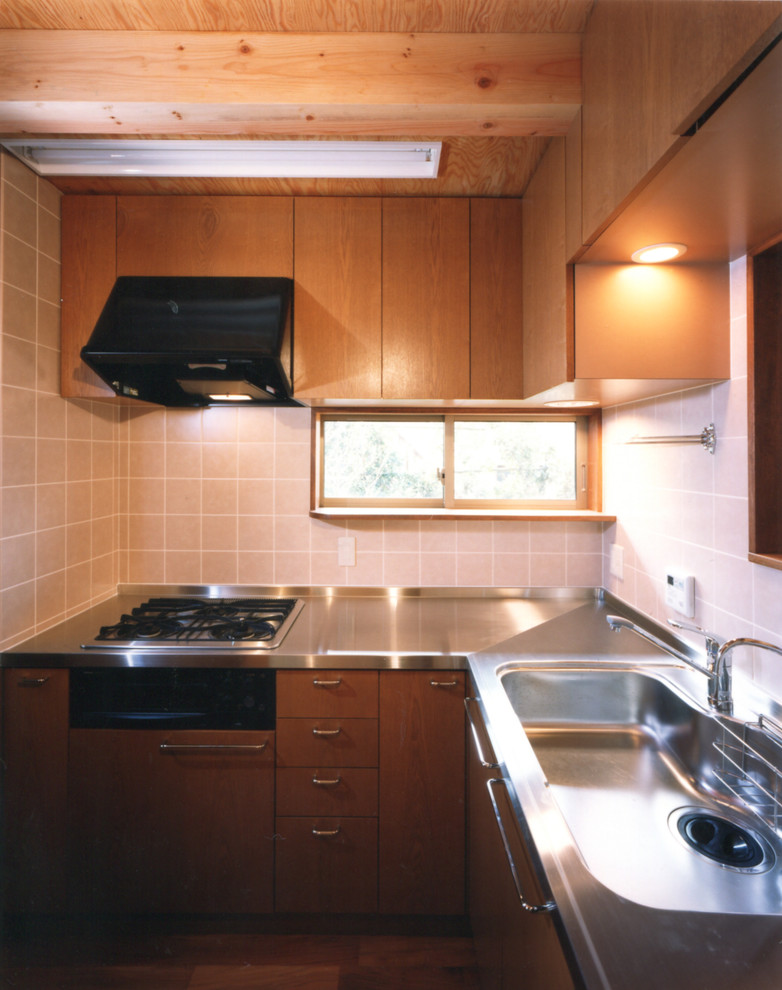 Small asian l-shaped separate kitchen in Tokyo with an integrated sink, beaded inset cabinets, medium wood cabinets, stainless steel benchtops, ceramic splashback, black appliances, medium hardwood floors, brown floor and pink splashback.
