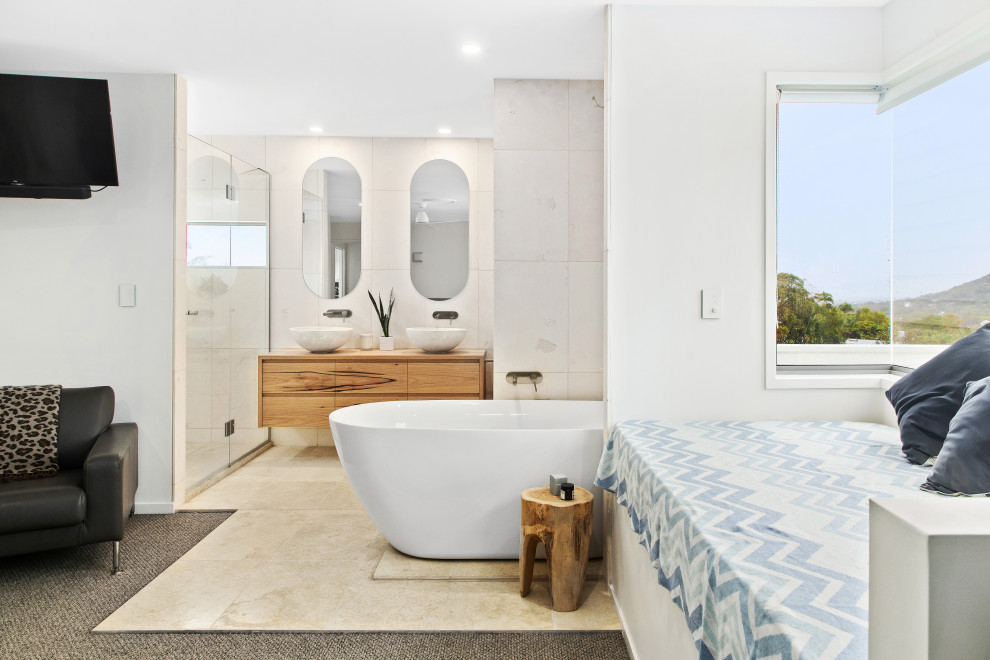 Cette image montre une salle de bain principale marine en bois clair de taille moyenne avec une baignoire indépendante, du carrelage en pierre calcaire, un sol en calcaire, des toilettes cachées, meuble double vasque et meuble-lavabo suspendu.