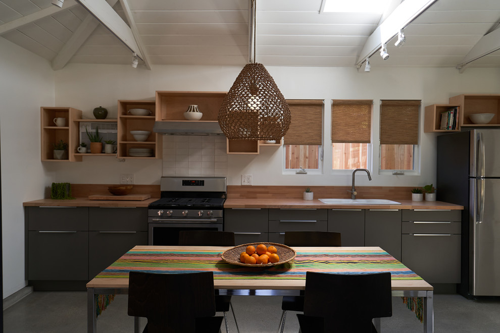 Inspiration for a small modern galley eat-in kitchen in Santa Barbara with a double-bowl sink, flat-panel cabinets, grey cabinets, wood benchtops, timber splashback, stainless steel appliances, concrete floors, with island, grey floor and multi-coloured benchtop.
