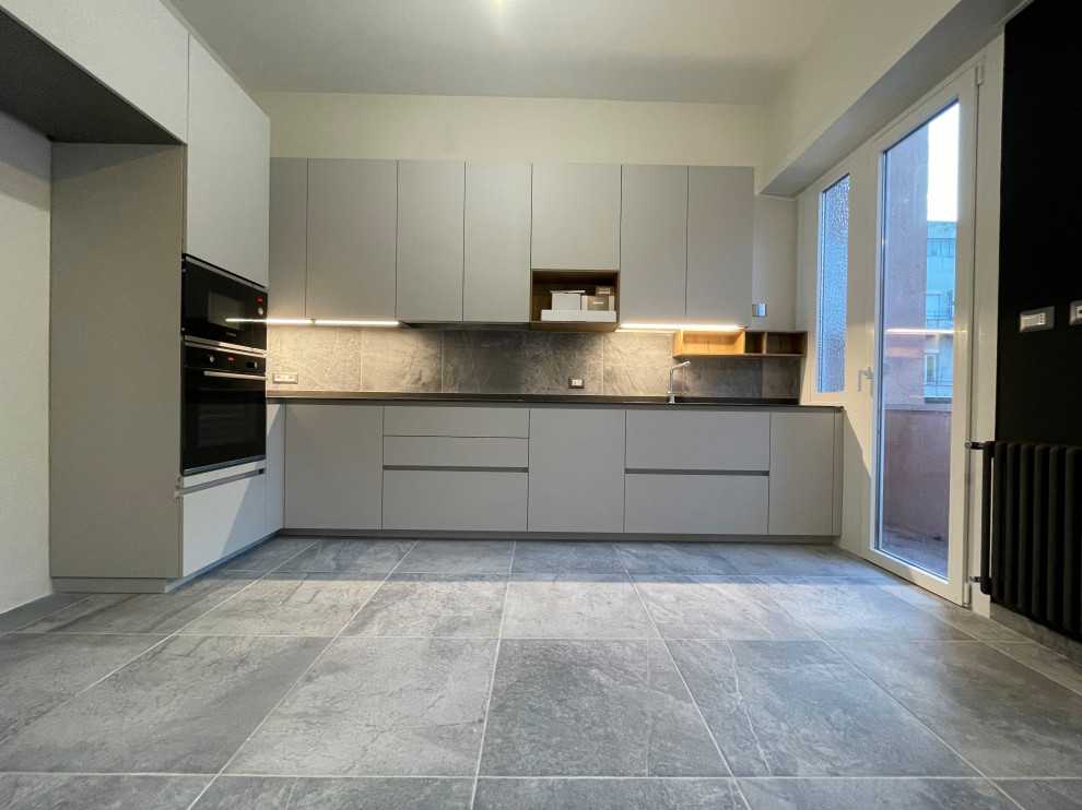 Design ideas for a large contemporary l-shaped separate kitchen in Rome with a drop-in sink, flat-panel cabinets, beige cabinets, quartzite benchtops, grey splashback, porcelain splashback, black appliances, porcelain floors, no island, grey floor and black benchtop.