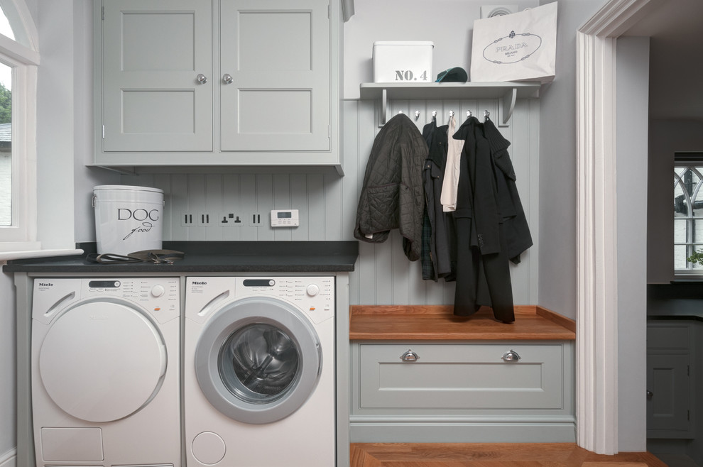 Design ideas for a small traditional single-wall utility room in Other with granite benchtops, grey walls, limestone floors, a side-by-side washer and dryer, black benchtop, beaded inset cabinets and grey cabinets.