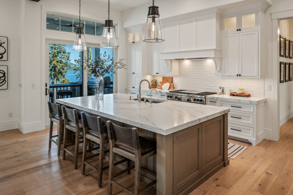 Photo of an expansive transitional open plan kitchen in San Francisco with an undermount sink, beaded inset cabinets, white cabinets, marble benchtops, white splashback, ceramic splashback, panelled appliances, light hardwood floors, with island, beige floor, white benchtop and exposed beam.