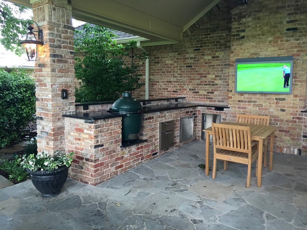This is an example of a mid-sized traditional backyard patio in Dallas with an outdoor kitchen, natural stone pavers and a roof extension.