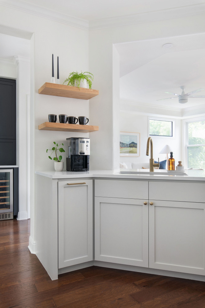 Home bar - mid-sized transitional medium tone wood floor and brown floor home bar idea in Austin with an undermount sink, shaker cabinets, gray cabinets, quartz countertops, white backsplash, brick backsplash and white countertops