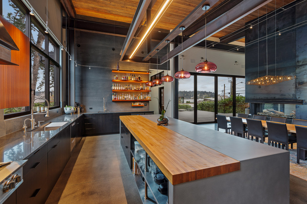 Inspiration for a large industrial l-shaped eat-in kitchen in Seattle with an undermount sink, flat-panel cabinets, black cabinets, concrete benchtops, grey splashback, porcelain splashback, stainless steel appliances, concrete floors, with island, grey floor, grey benchtop and wood.