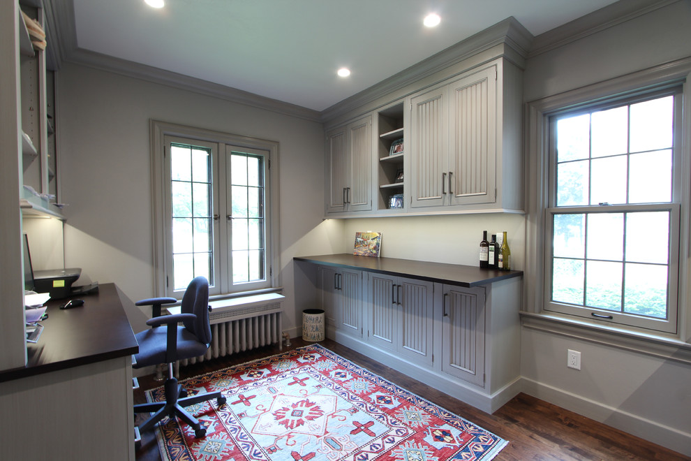 This is an example of a large transitional home office in Other with grey walls, medium hardwood floors, a built-in desk and brown floor.