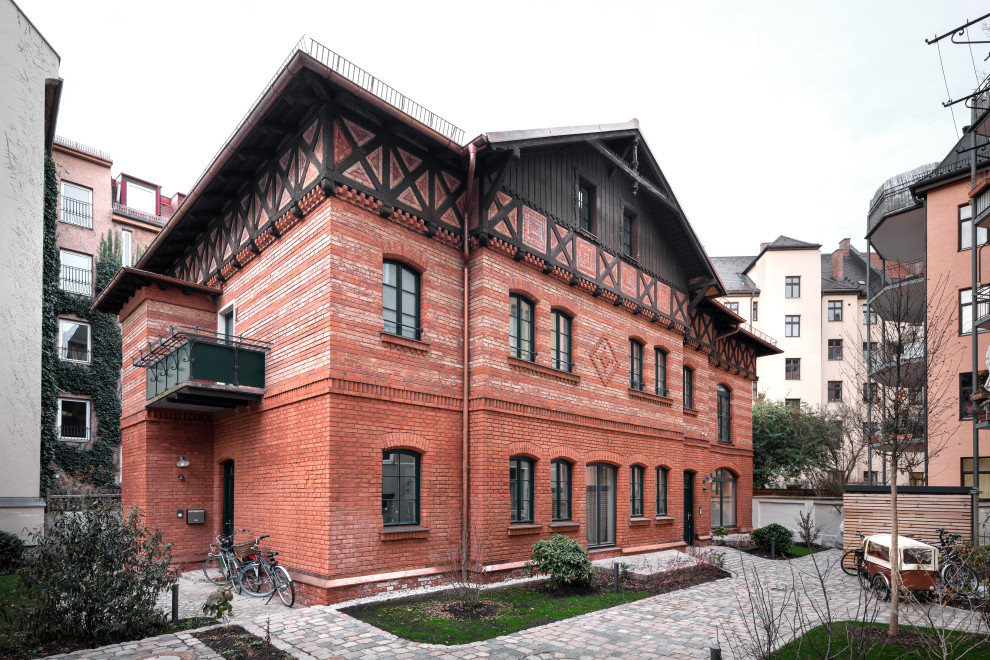 Large country two-storey brick red apartment exterior in Munich with a hip roof and a metal roof.