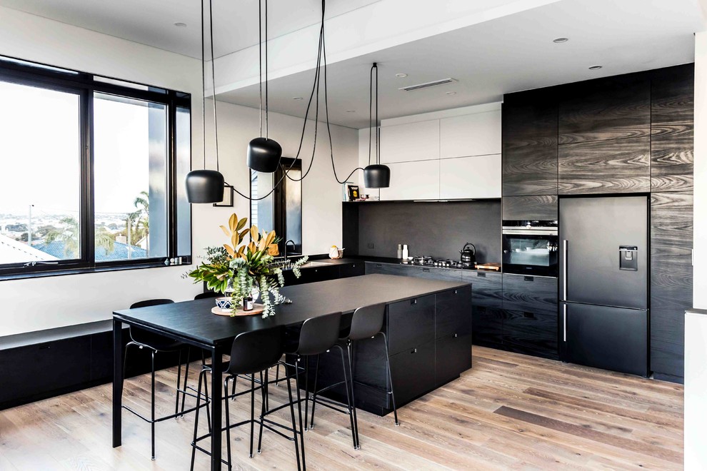 Photo of a large scandinavian l-shaped open plan kitchen in Perth with black splashback, with island, flat-panel cabinets, black appliances, a drop-in sink, black cabinets and light hardwood floors.