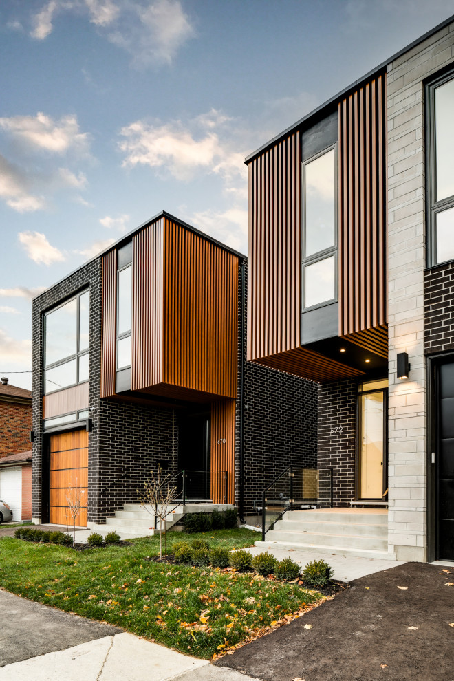 This is an example of a small modern two-storey brick black house exterior in Toronto with a flat roof and board and batten siding.