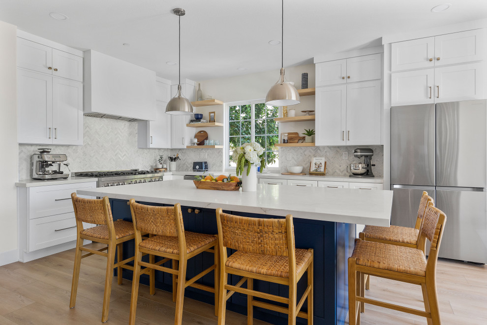 Mid-sized minimalist l-shaped light wood floor and brown floor eat-in kitchen photo in Orange County with a farmhouse sink, recessed-panel cabinets, white cabinets, marble countertops, white backsplash, stainless steel appliances, an island and white countertops