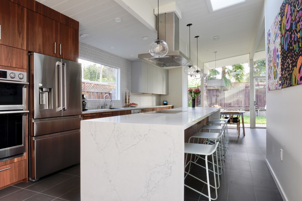 This is an example of a large modern single-wall eat-in kitchen in San Francisco with medium wood cabinets, white splashback, ceramic splashback, stainless steel appliances, ceramic floors, a peninsula, grey floor and white benchtop.