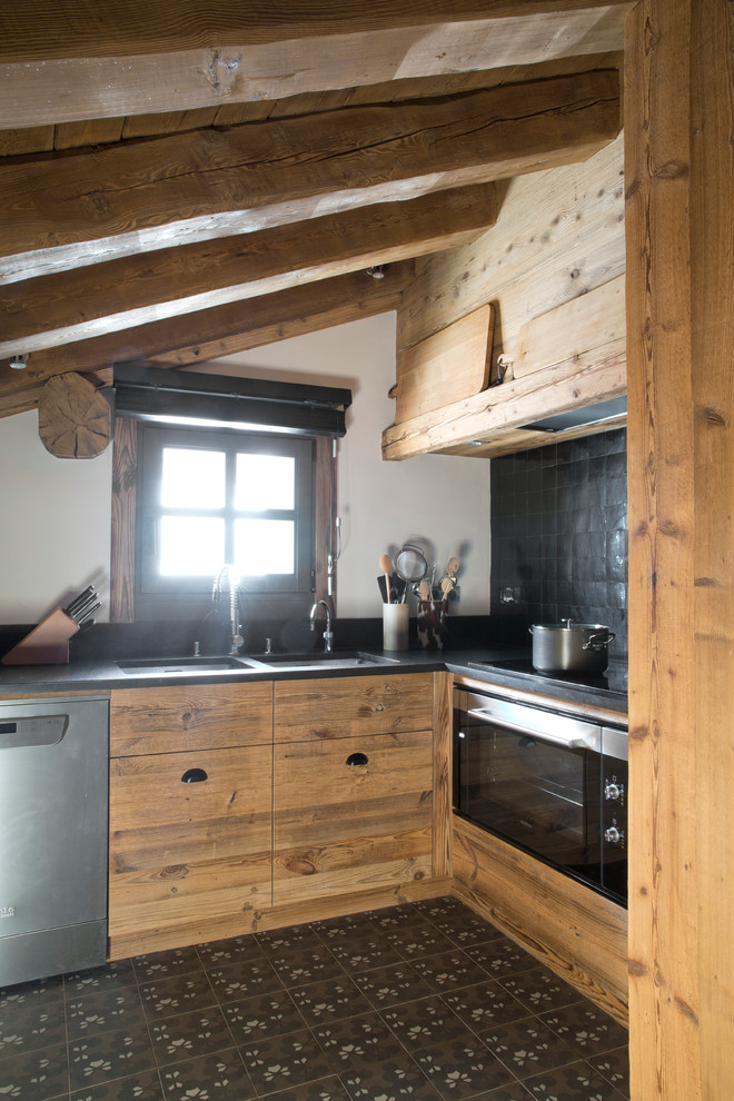 This is an example of a mid-sized country l-shaped separate kitchen in Lyon with a double-bowl sink, light wood cabinets, black splashback, stainless steel appliances, cement tiles and black floor.