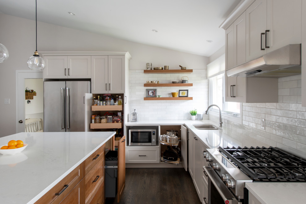 Inspiration for a mid-sized transitional l-shaped medium tone wood floor, gray floor and vaulted ceiling open concept kitchen remodel in Ottawa with a double-bowl sink, shaker cabinets, gray cabinets, quartz countertops, white backsplash, subway tile backsplash, stainless steel appliances, an island and white countertops