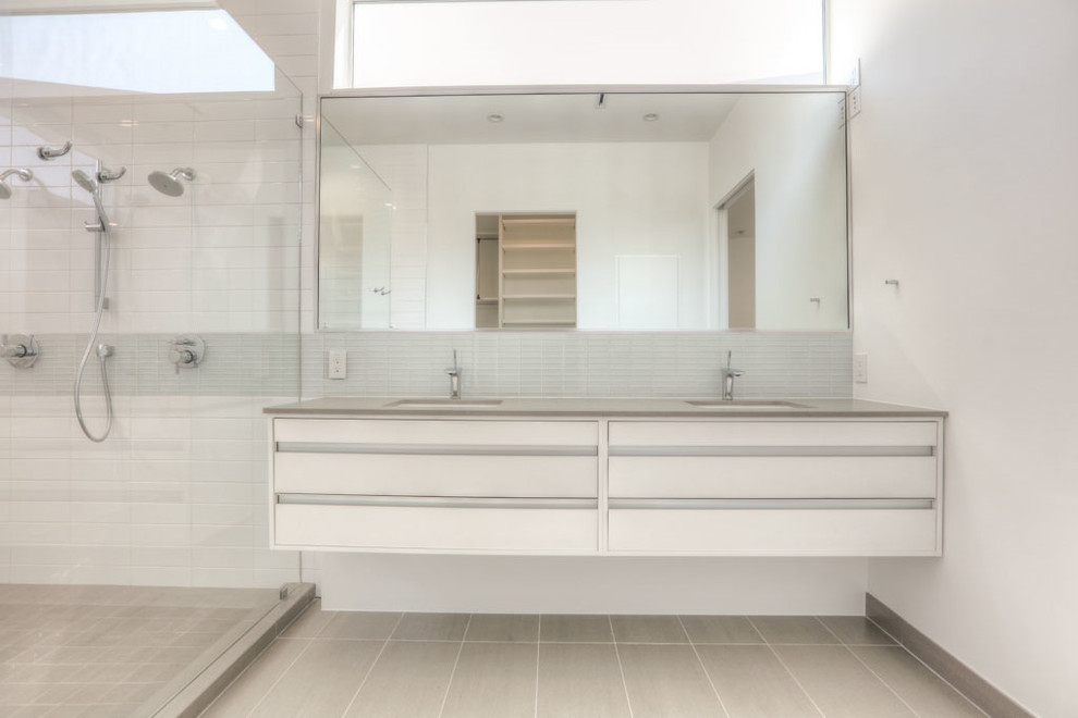 This is an example of a mid-sized modern master bathroom in Houston with flat-panel cabinets, white cabinets, a freestanding tub, an alcove shower, a one-piece toilet, gray tile, mosaic tile, white walls, ceramic floors, an undermount sink, solid surface benchtops, grey floor and a hinged shower door.