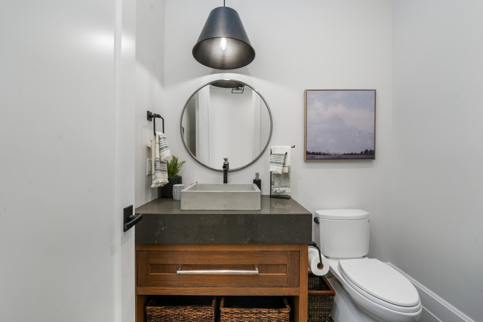 Foto på ett litet vintage vit toalett, med luckor med infälld panel, bruna skåp, en toalettstol med separat cisternkåpa, vit kakel, porslinskakel, vita väggar, klinkergolv i porslin, ett undermonterad handfat, bänkskiva i kvarts och grått golv