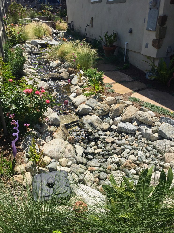 This is an example of a mid-sized country front yard full sun formal garden for spring in San Diego with a retaining wall and natural stone pavers.