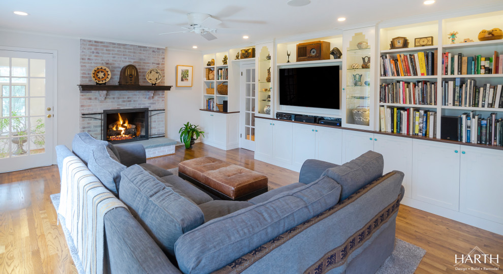 This is an example of a mid-sized transitional open concept family room in Philadelphia with white walls, medium hardwood floors, a standard fireplace, a brick fireplace surround, a wall-mounted tv and brown floor.