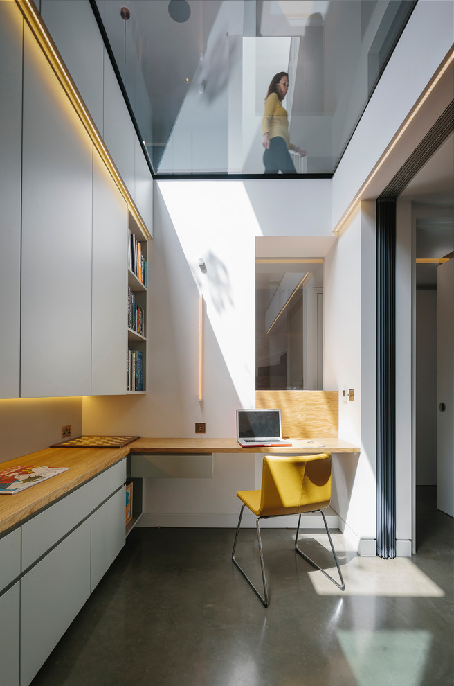 This is an example of a contemporary study room in London with white walls, concrete floors and a built-in desk.