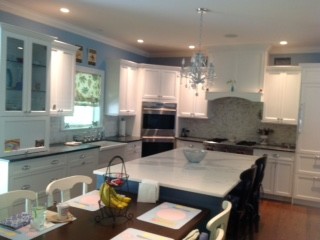 Kitchen - transitional medium tone wood floor kitchen idea in New York with a farmhouse sink, recessed-panel cabinets, white cabinets, marble countertops, white backsplash, stone tile backsplash, paneled appliances and an island