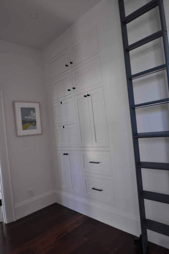 Aménagement d'une petite armoire encastrée classique avec un placard avec porte à panneau encastré, des portes de placard blanches, parquet foncé et un sol marron.
