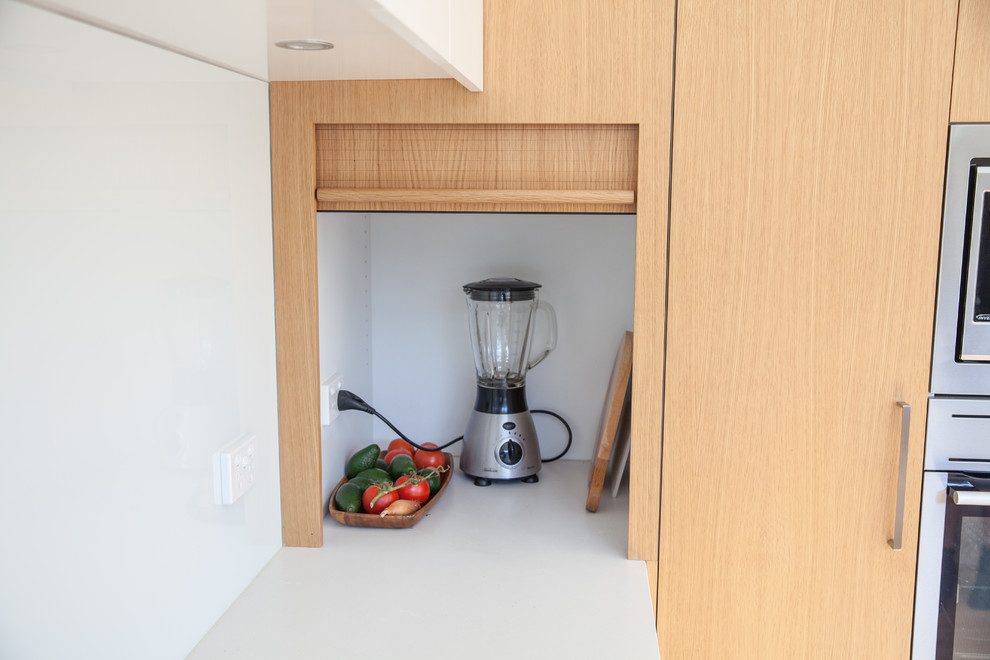 Photo of a mid-sized scandinavian u-shaped eat-in kitchen in Melbourne with an undermount sink, flat-panel cabinets, white cabinets, granite benchtops, white splashback, glass sheet splashback, a peninsula, stainless steel appliances, light hardwood floors and grey benchtop.