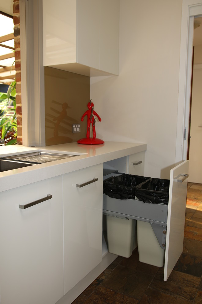 This is an example of a large modern galley kitchen pantry in Sydney with an undermount sink, flat-panel cabinets, white cabinets, quartz benchtops, brown splashback, glass sheet splashback, stainless steel appliances, slate floors and no island.