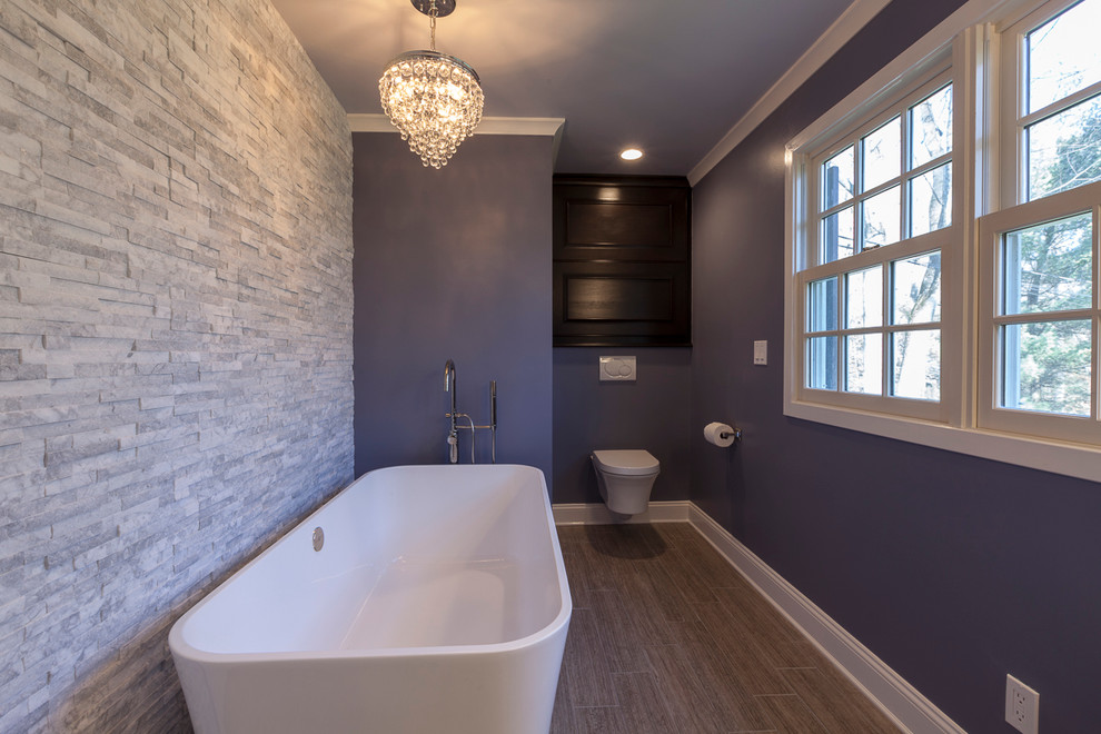 This is an example of a large contemporary master bathroom in New York with a freestanding tub, flat-panel cabinets, dark wood cabinets, a curbless shower, a wall-mount toilet, white tile, porcelain tile, purple walls, porcelain floors, an undermount sink, engineered quartz benchtops, grey floor and an open shower.
