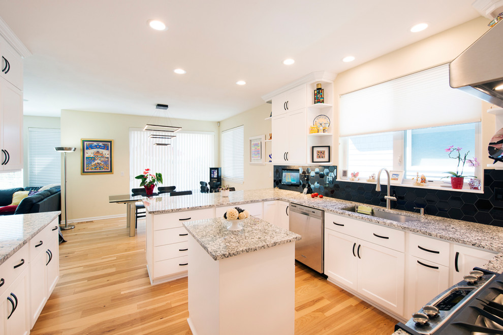 This is an example of a mid-sized transitional u-shaped eat-in kitchen in Portland with an undermount sink, shaker cabinets, white cabinets, granite benchtops, black splashback, ceramic splashback, stainless steel appliances, light hardwood floors, with island, brown floor and grey benchtop.