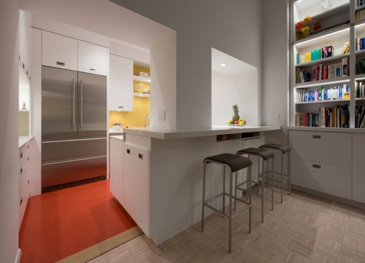 This is an example of a small modern u-shaped separate kitchen in New York with an undermount sink, flat-panel cabinets, white cabinets, solid surface benchtops, yellow splashback, glass sheet splashback, stainless steel appliances, linoleum floors, a peninsula and red floor.