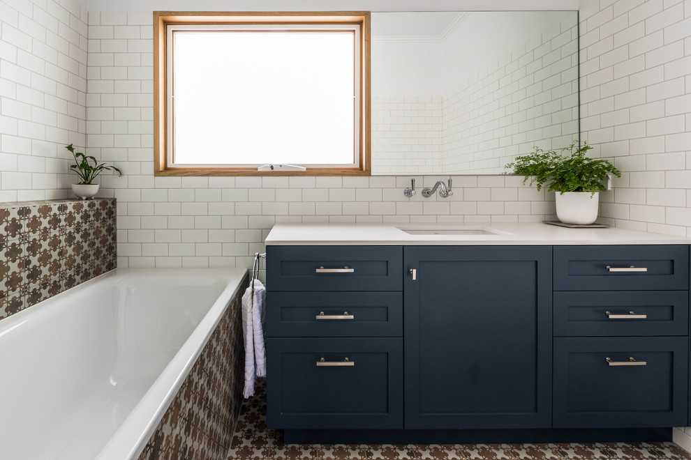 Inspiration for a transitional 3/4 bathroom in Melbourne with shaker cabinets, blue cabinets, a drop-in tub, white tile, ceramic tile, white walls, cement tiles, an undermount sink, multi-coloured floor and beige benchtops.