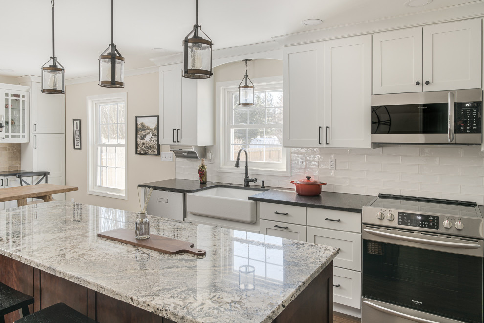 Mid-sized transitional u-shaped brown floor eat-in kitchen photo in Boston with a farmhouse sink, recessed-panel cabinets, white cabinets, granite countertops, white backsplash, porcelain backsplash, stainless steel appliances, an island and black countertops