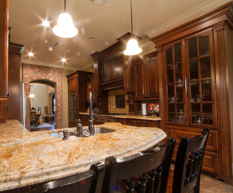 Mid-sized traditional galley separate kitchen in New Orleans with a drop-in sink, shaker cabinets, medium wood cabinets, marble benchtops, beige splashback, travertine splashback, stainless steel appliances, travertine floors, no island and brown floor.