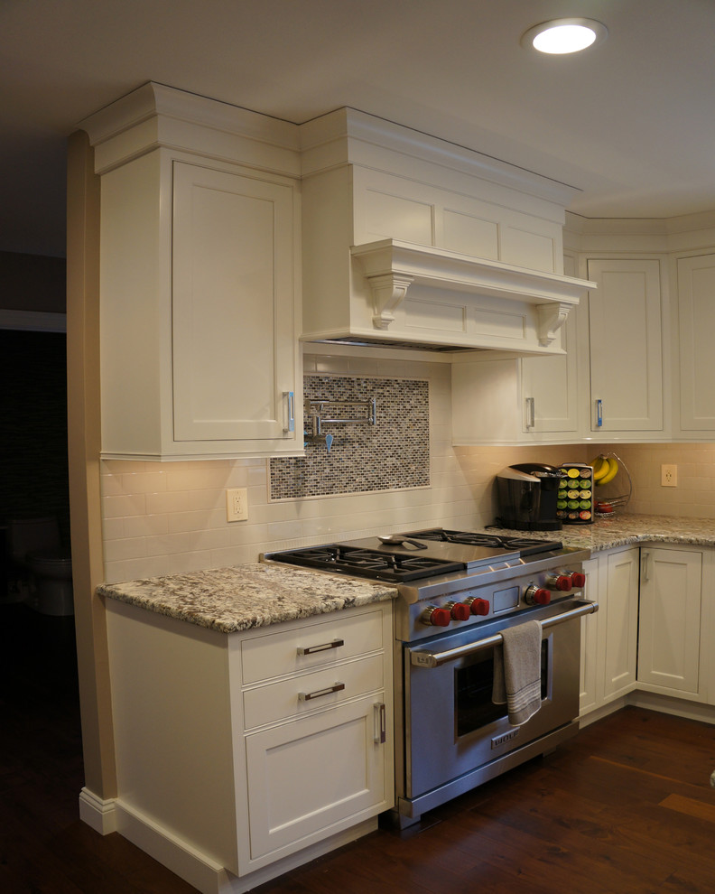 Example of a large l-shaped medium tone wood floor enclosed kitchen design in Boston with white cabinets, white backsplash, stainless steel appliances, an island, recessed-panel cabinets, granite countertops and subway tile backsplash
