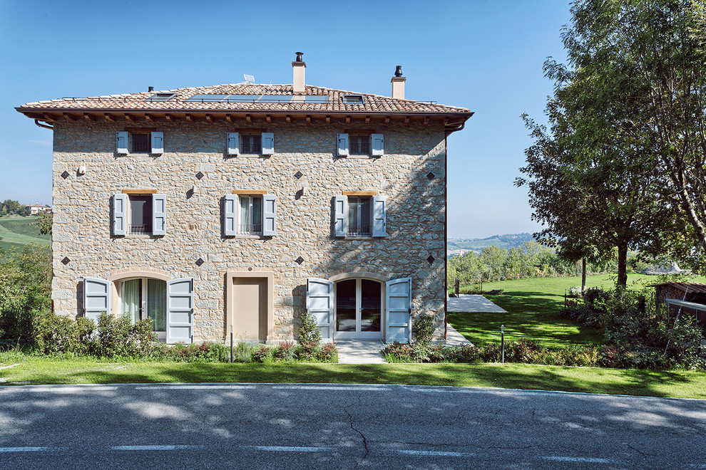 Large country three-storey beige duplex exterior in Bologna with stone veneer and a tile roof.
