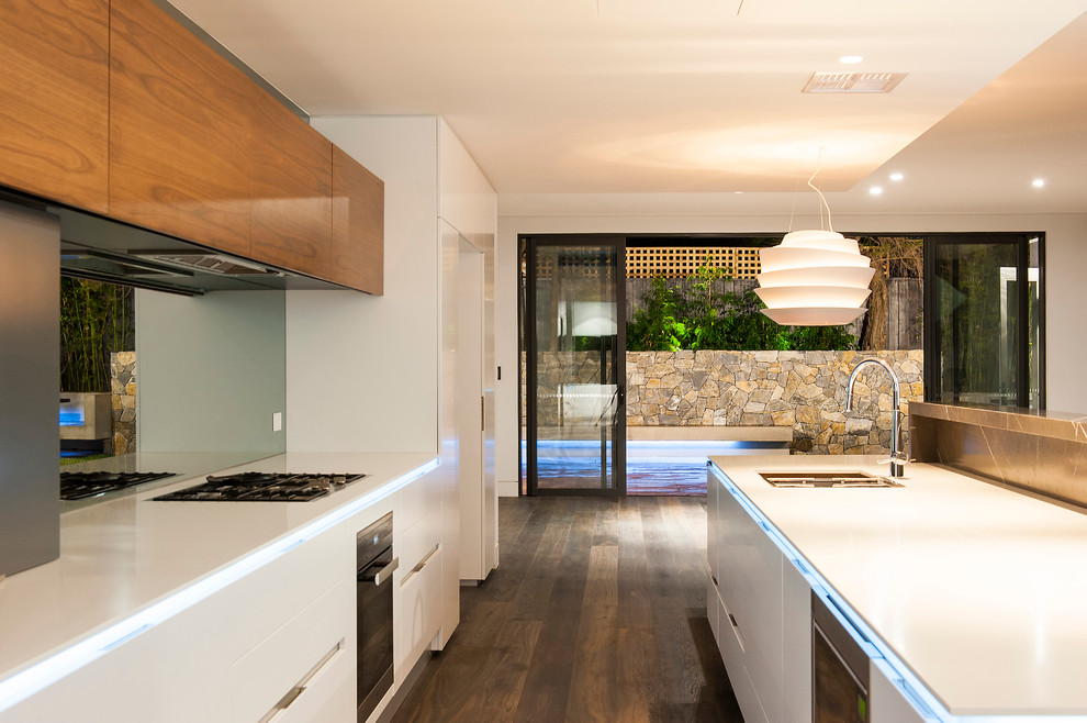 Large contemporary galley eat-in kitchen in Sydney with an undermount sink, white cabinets, solid surface benchtops, mirror splashback, stainless steel appliances, dark hardwood floors and with island.