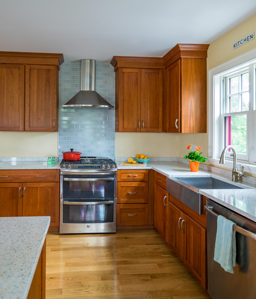 Mid-sized beach style l-shaped eat-in kitchen in Boston with a farmhouse sink, shaker cabinets, medium wood cabinets, quartz benchtops, blue splashback, subway tile splashback, stainless steel appliances, light hardwood floors and with island.