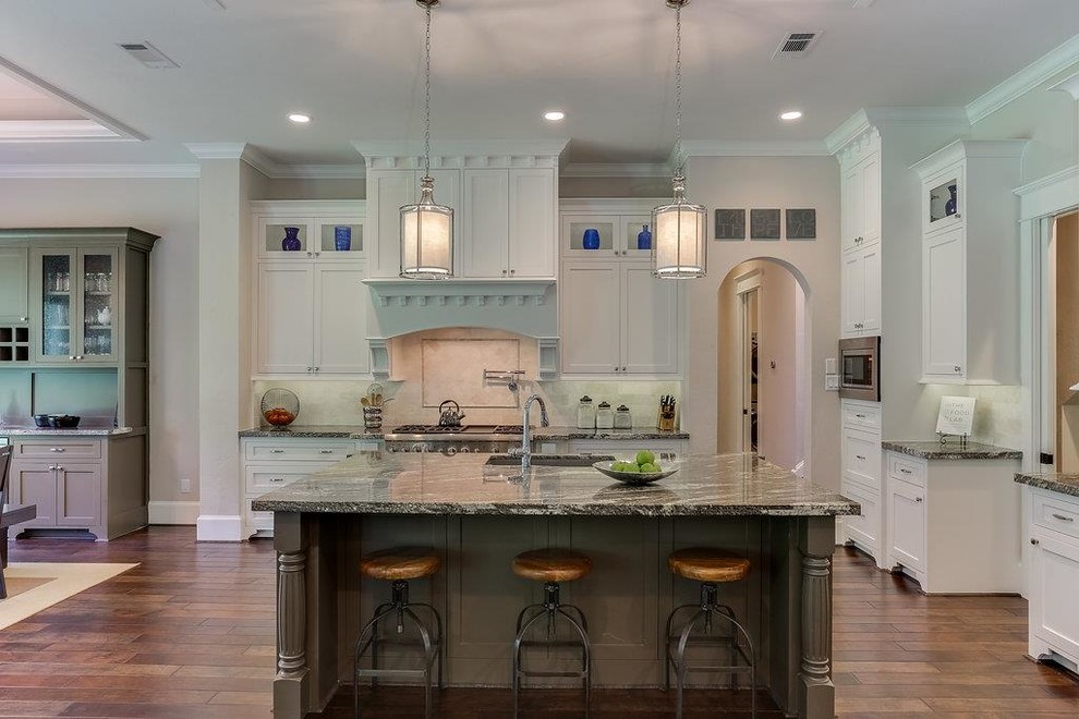 This is an example of a mid-sized arts and crafts l-shaped open plan kitchen in Houston with an undermount sink, shaker cabinets, white cabinets, granite benchtops, beige splashback, ceramic splashback, stainless steel appliances, medium hardwood floors, with island and multi-coloured floor.