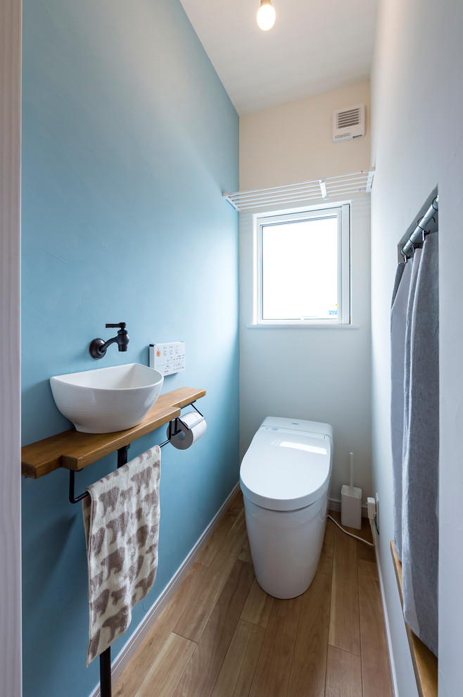 Photo of a small scandinavian powder room in Other with blue walls, medium hardwood floors, a vessel sink, wood benchtops, brown floor and brown benchtops.