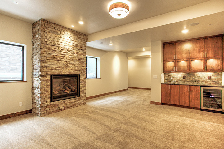 Inspiration for a mid-sized rustic look-out carpeted basement remodel in Denver with beige walls, a standard fireplace and a stone fireplace