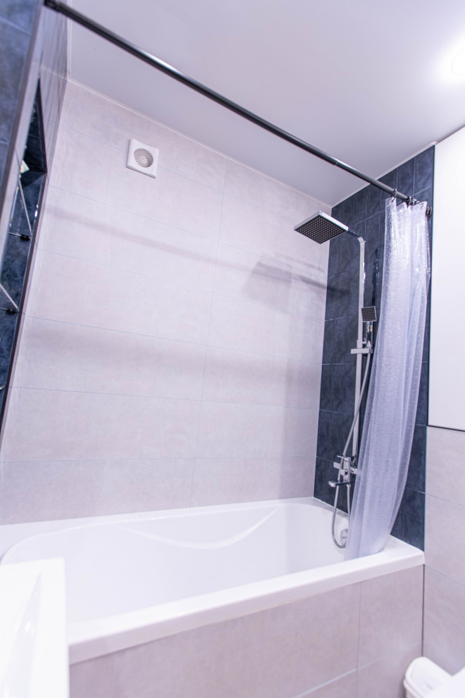 Modern inredning av ett litet en-suite badrum, med släta luckor, skåp i mellenmörkt trä, ett badkar i en alkov, en dusch/badkar-kombination, en vägghängd toalettstol, blå kakel, beige väggar, klinkergolv i porslin, ett nedsänkt handfat, grått golv och dusch med duschdraperi