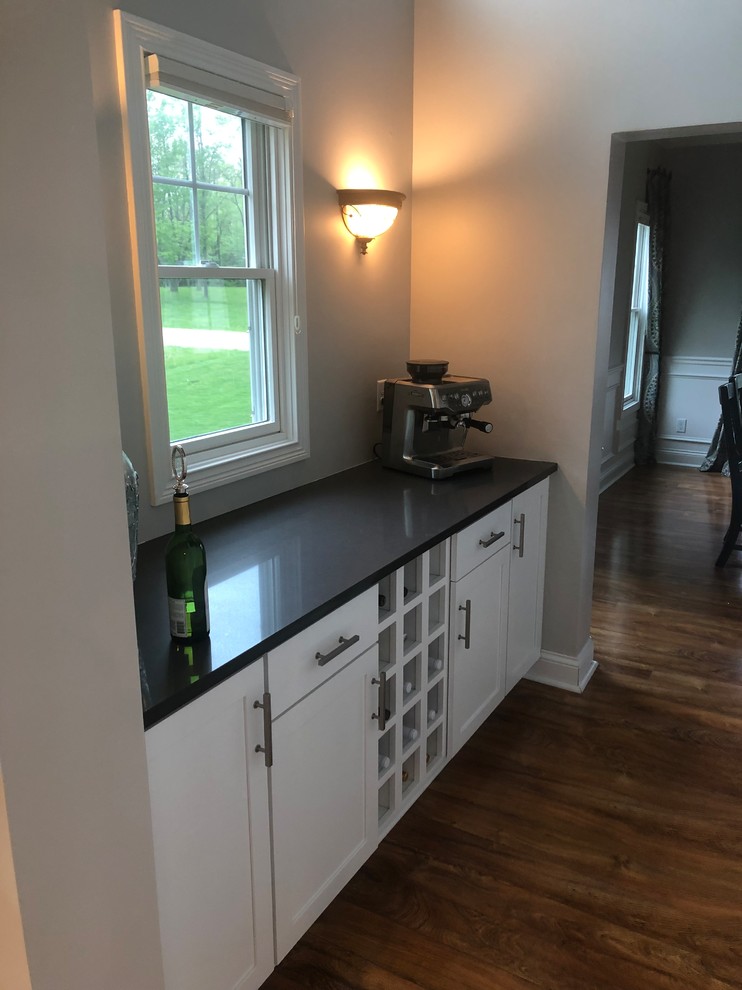Kitchen - laminate floor and brown floor kitchen idea with a single-bowl sink, shaker cabinets, white cabinets, quartzite countertops, white backsplash, subway tile backsplash, stainless steel appliances, an island and gray countertops