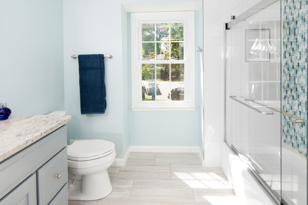 Design ideas for a mid-sized contemporary bathroom in DC Metro with recessed-panel cabinets, grey cabinets, an alcove tub, a shower/bathtub combo, a two-piece toilet, blue tile, matchstick tile, blue walls, porcelain floors, granite benchtops, beige floor and a sliding shower screen.