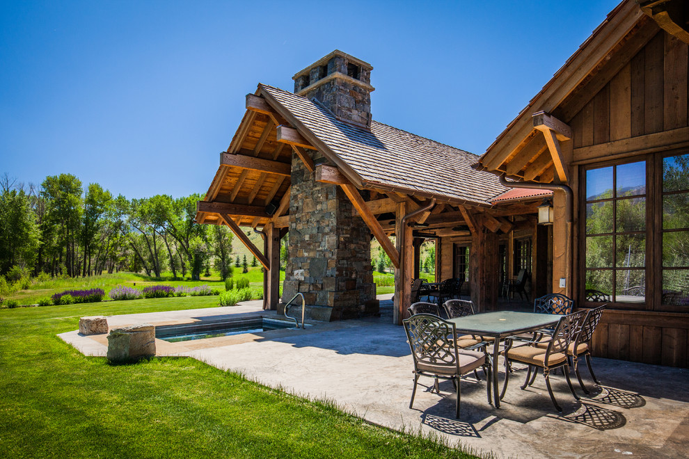 Example of a large mountain style backyard concrete patio fountain design with a roof extension