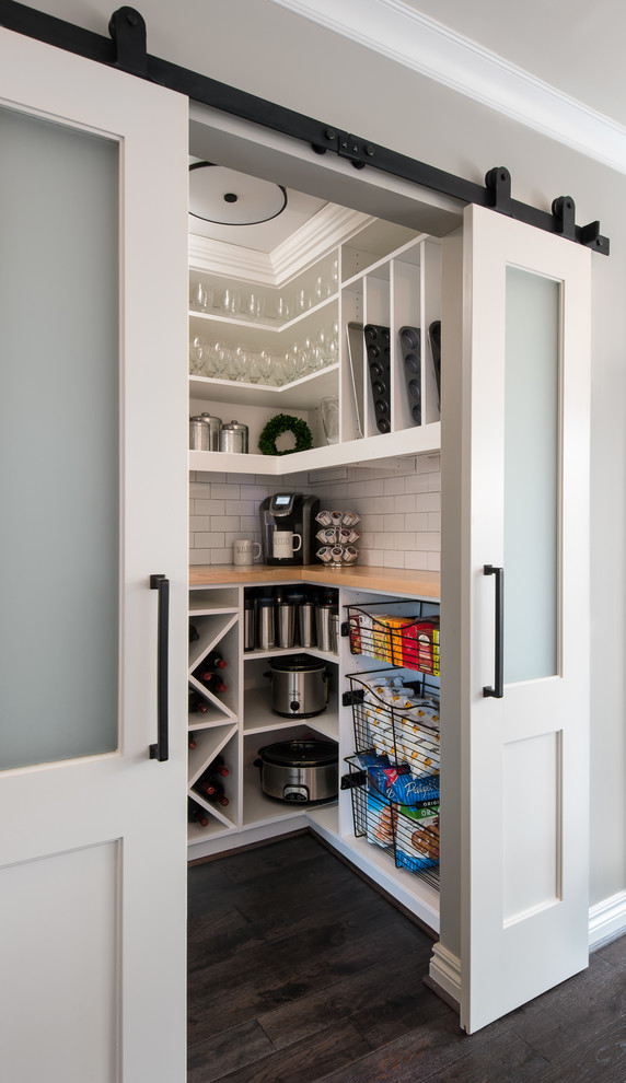 This is an example of a small transitional kitchen pantry in Detroit with white cabinets, white splashback, subway tile splashback, stainless steel appliances, dark hardwood floors, a farmhouse sink, wood benchtops, brown floor, white benchtop and open cabinets.