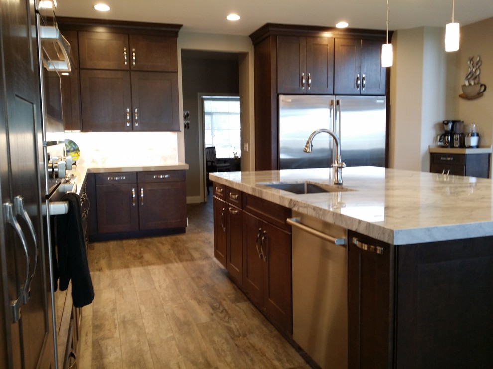 Large transitional l-shaped open plan kitchen in Las Vegas with an undermount sink, shaker cabinets, brown cabinets, quartzite benchtops, white splashback, marble splashback, stainless steel appliances, porcelain floors, with island, multi-coloured floor and grey benchtop.