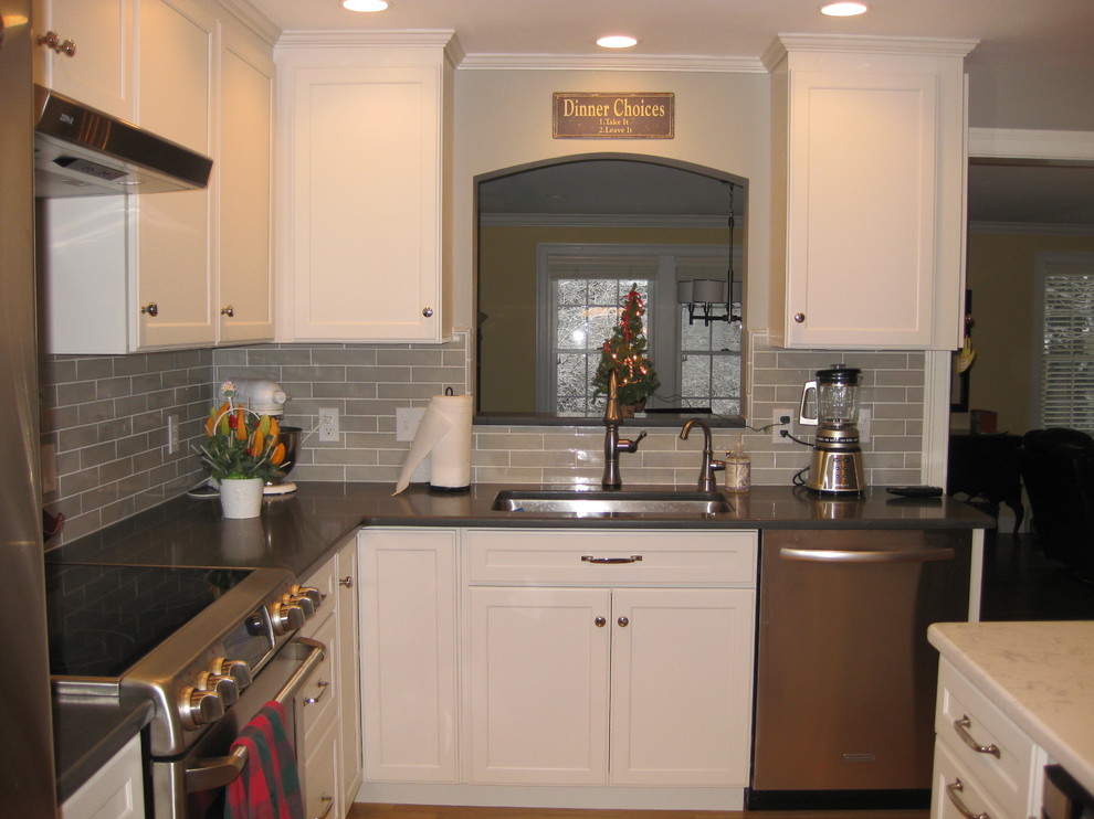 Example of a transitional l-shaped medium tone wood floor eat-in kitchen design in Boston with an undermount sink, white cabinets, quartz countertops, stainless steel appliances, an island, shaker cabinets, green backsplash, subway tile backsplash and black countertops